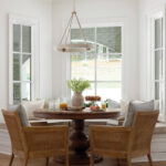 Breakfast nook with round wooden table, cane chairs, and bay windows.