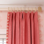 Coral curtains with fringe trim and floral wallpaper