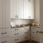 Pantry with cream vertical-paneled cabinetry, black hardware, and a stone countertop.