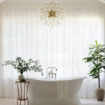 White freestanding bathtub with chrome fixtures, under a crystal chandelier.