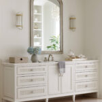 White bathroom vanity with marble countertop, silver faucet, and decorative sconces.