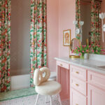 Pink bathroom with floral curtains, patterned floor tiles, and a white boucle vanity stool.