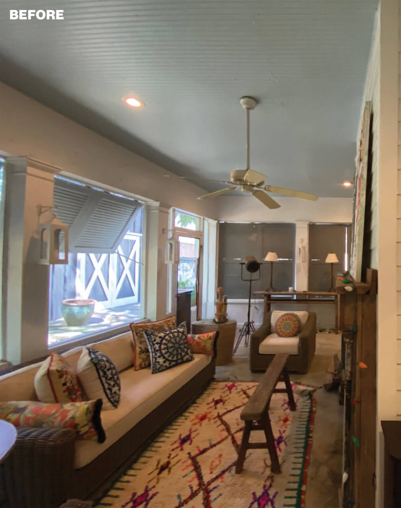 Sunroom with beige sofa, colorful patterned rug, armchair, and ceiling fan.