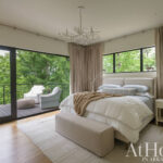 Bedroom with large windows, beige curtains, and a wooden bed.