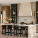 Kitchen island with marble countertop, dark cabinetry, and a large hood.