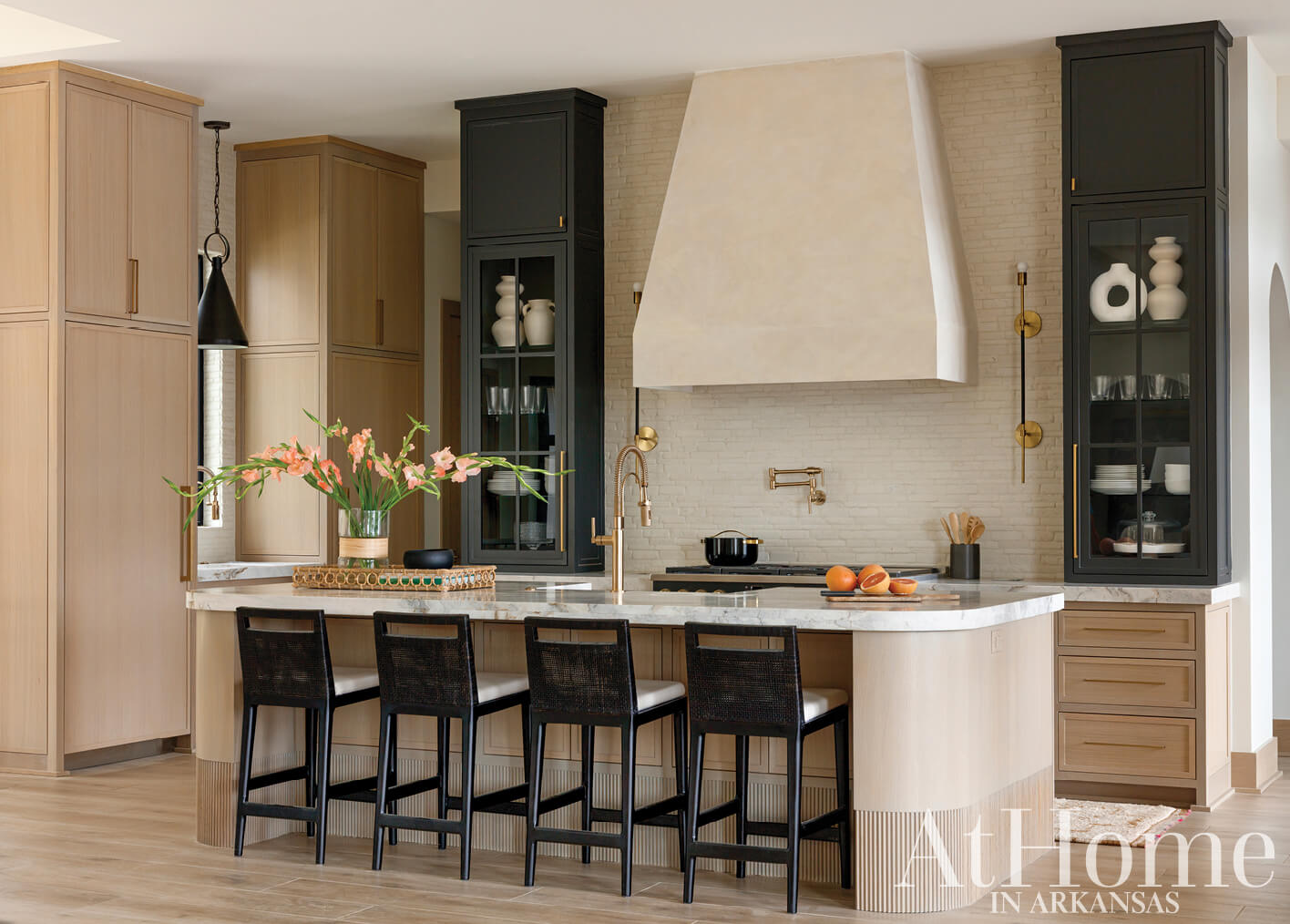 Kitchen island with marble countertop, dark cabinetry, and a large hood.