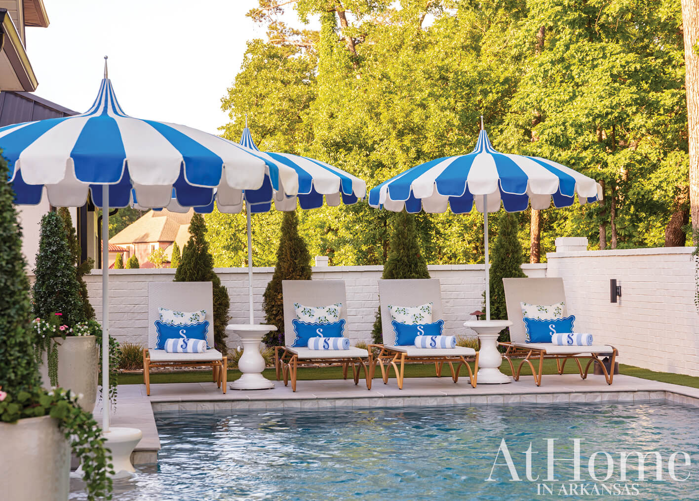 Blue and white striped umbrellas shade outdoor lounge chairs by a pool.