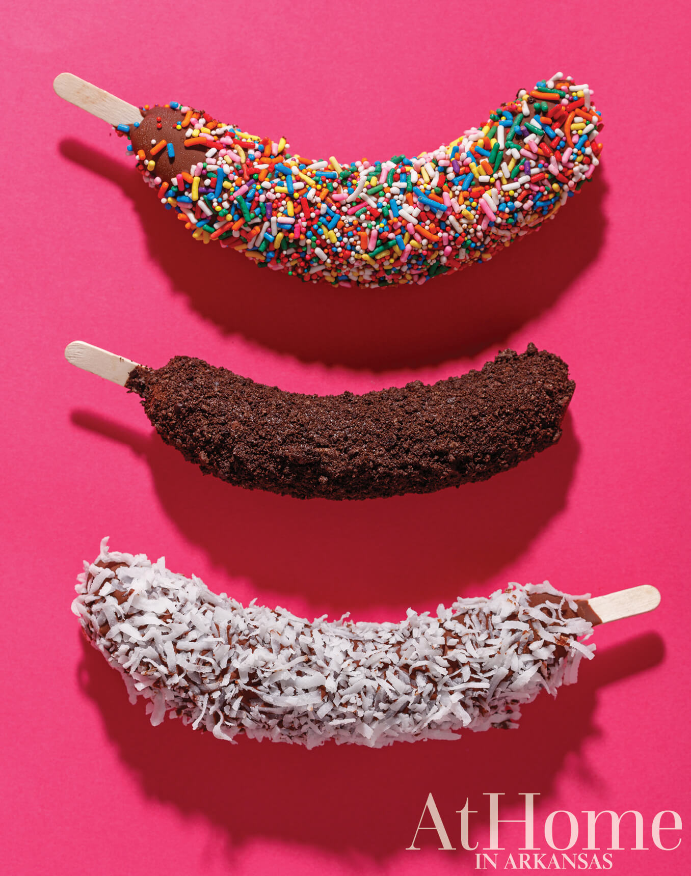 Three chocolate-covered bananas with different toppings: sprinkles, cocoa, and coconut.