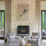Stone fireplace with gray upholstered armchairs and a painting.