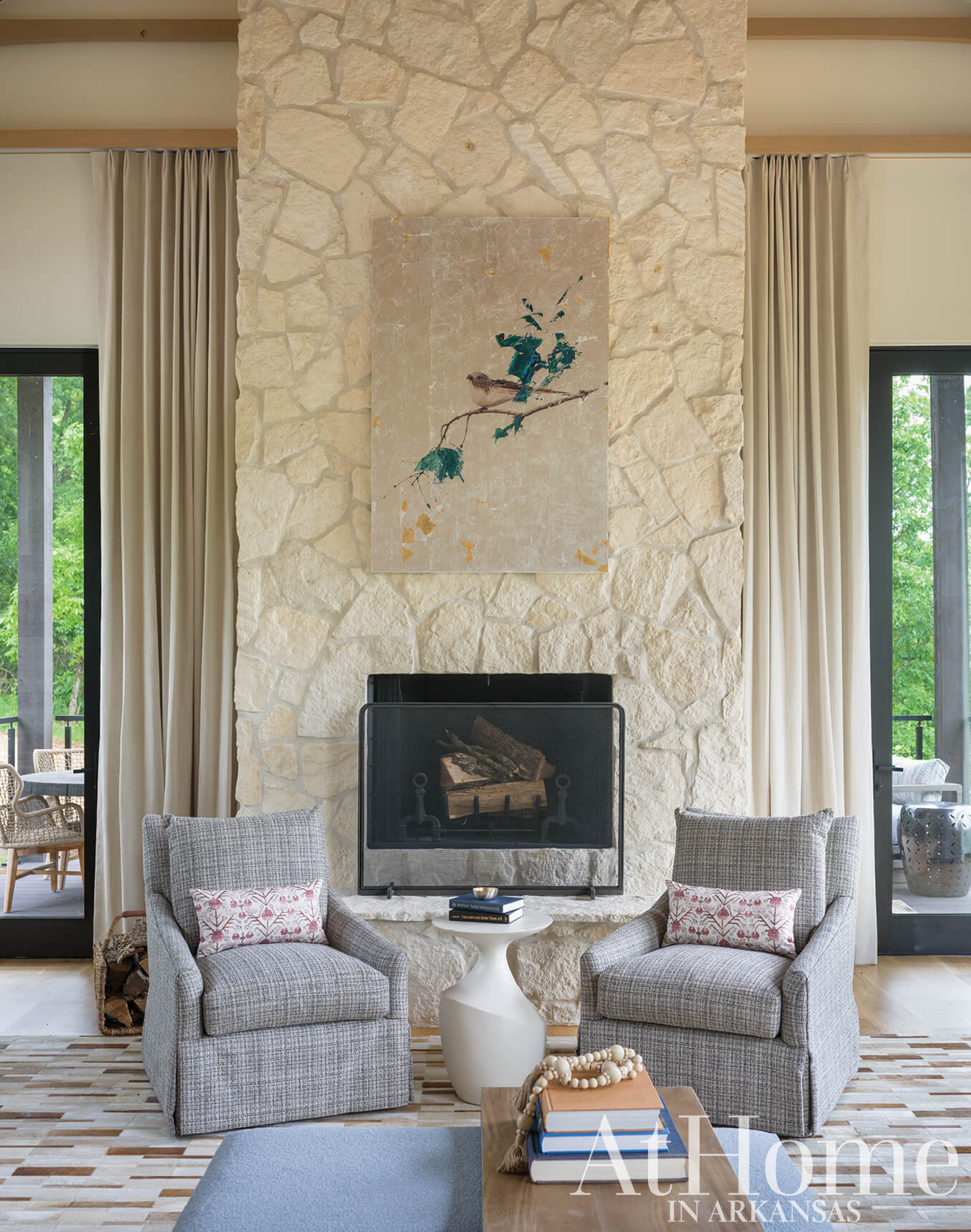 Stone fireplace with gray upholstered armchairs and a painting.