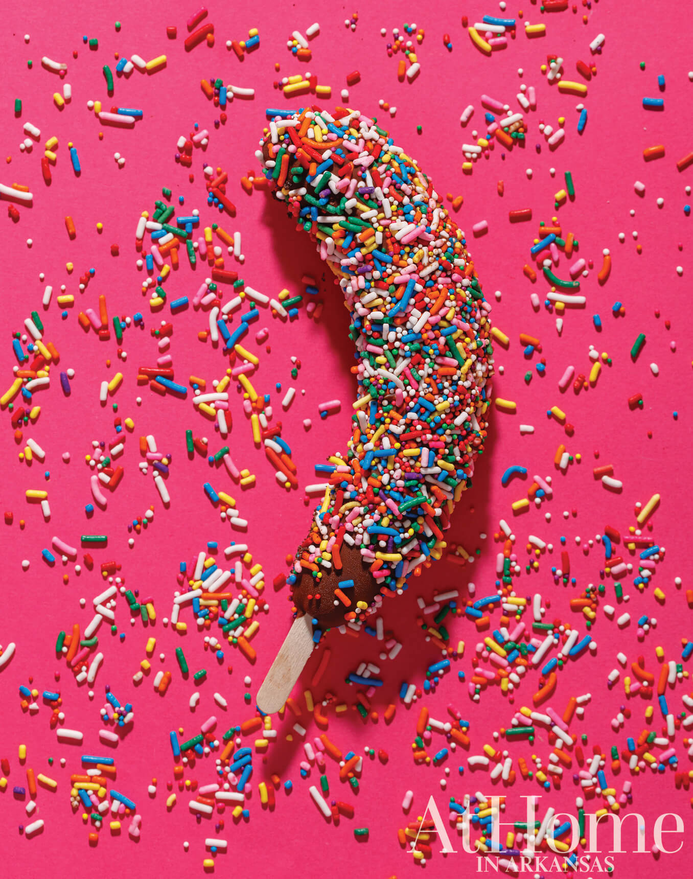 Banana covered in colorful sprinkles on pink background.