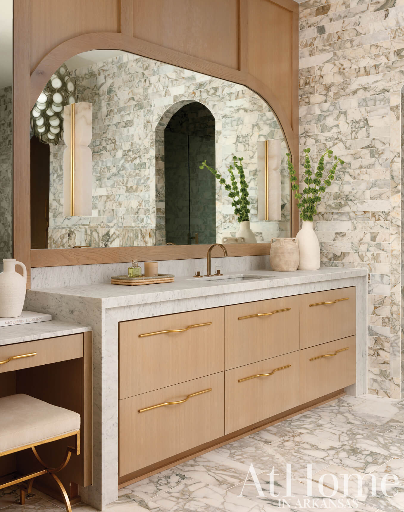 Marble and wood vanity with arched mirror and brass fixtures.