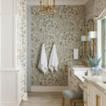 Bathroom with floral wallpaper, gold accents, and white cabinetry.