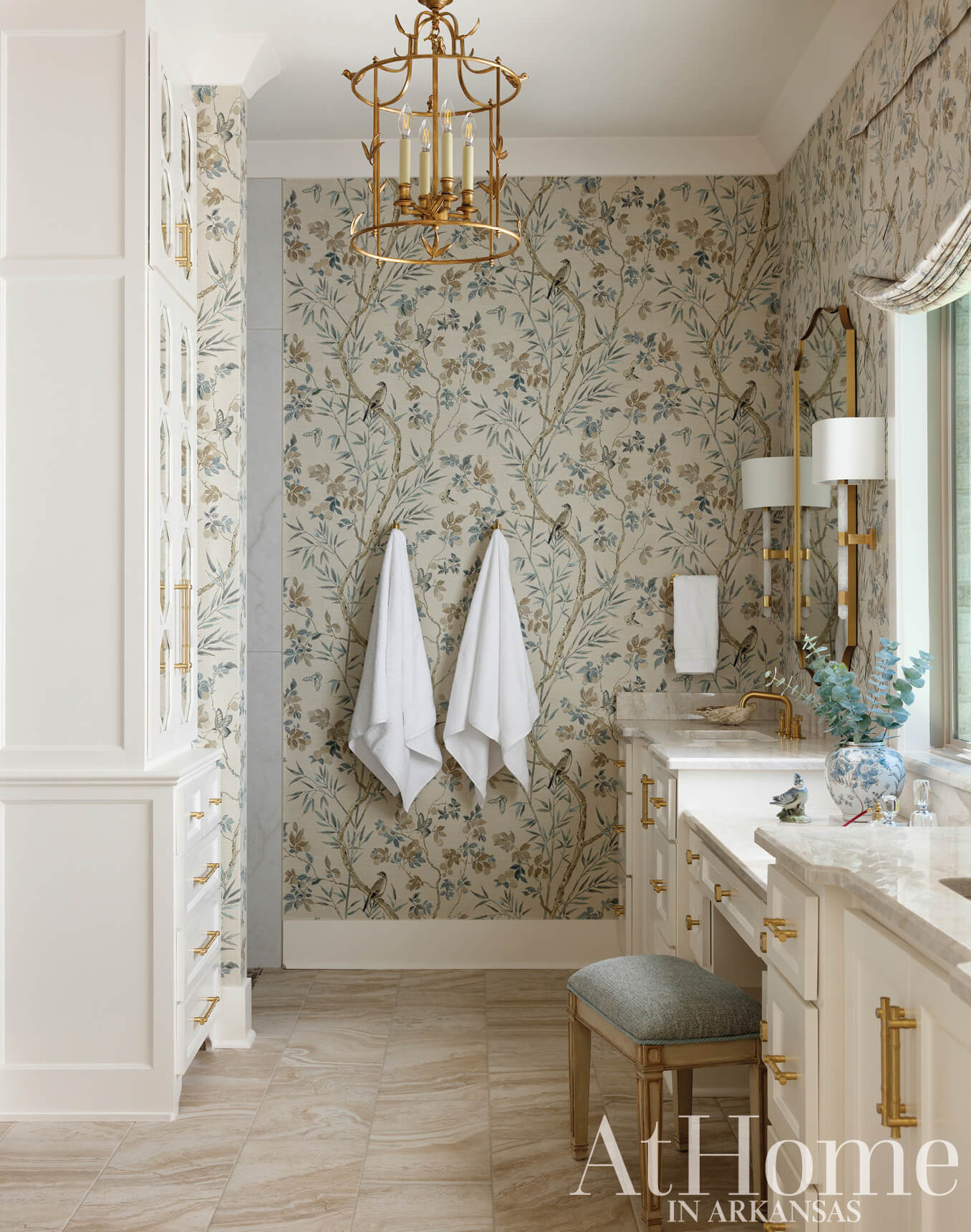 Bathroom with floral wallpaper, gold accents, and white cabinetry.