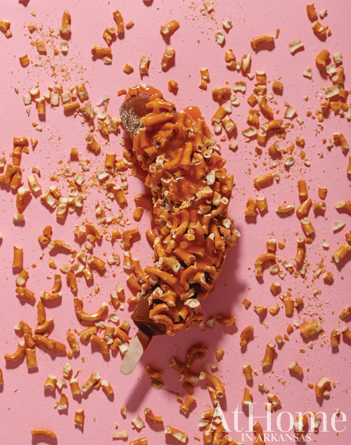 Ice cream stick covered in caramel and broken pretzels.