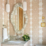 Bathroom with patterned wallpaper, mirror, and sconces.