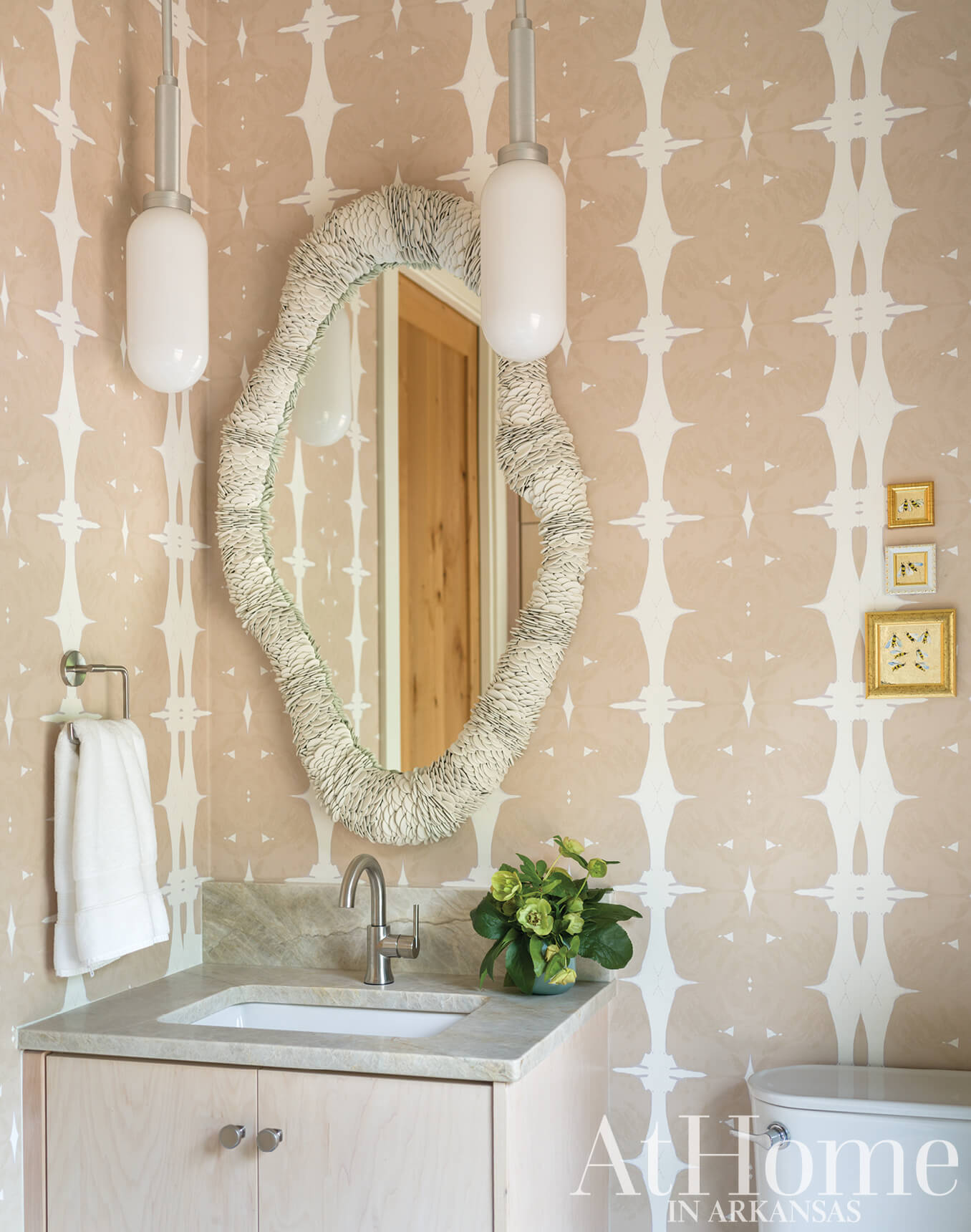 Bathroom with patterned wallpaper, mirror, and sconces.