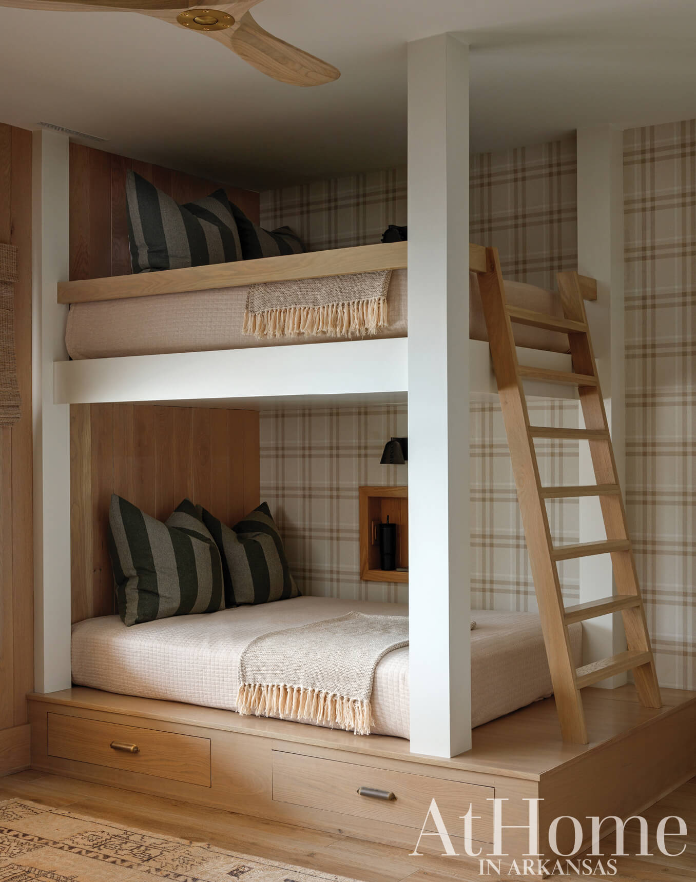 Two-tiered bunk bed with plaid wallpaper and wooden ladder.