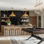 Modern kitchen with black tile backsplash, gold pendant lights, and a pool table.