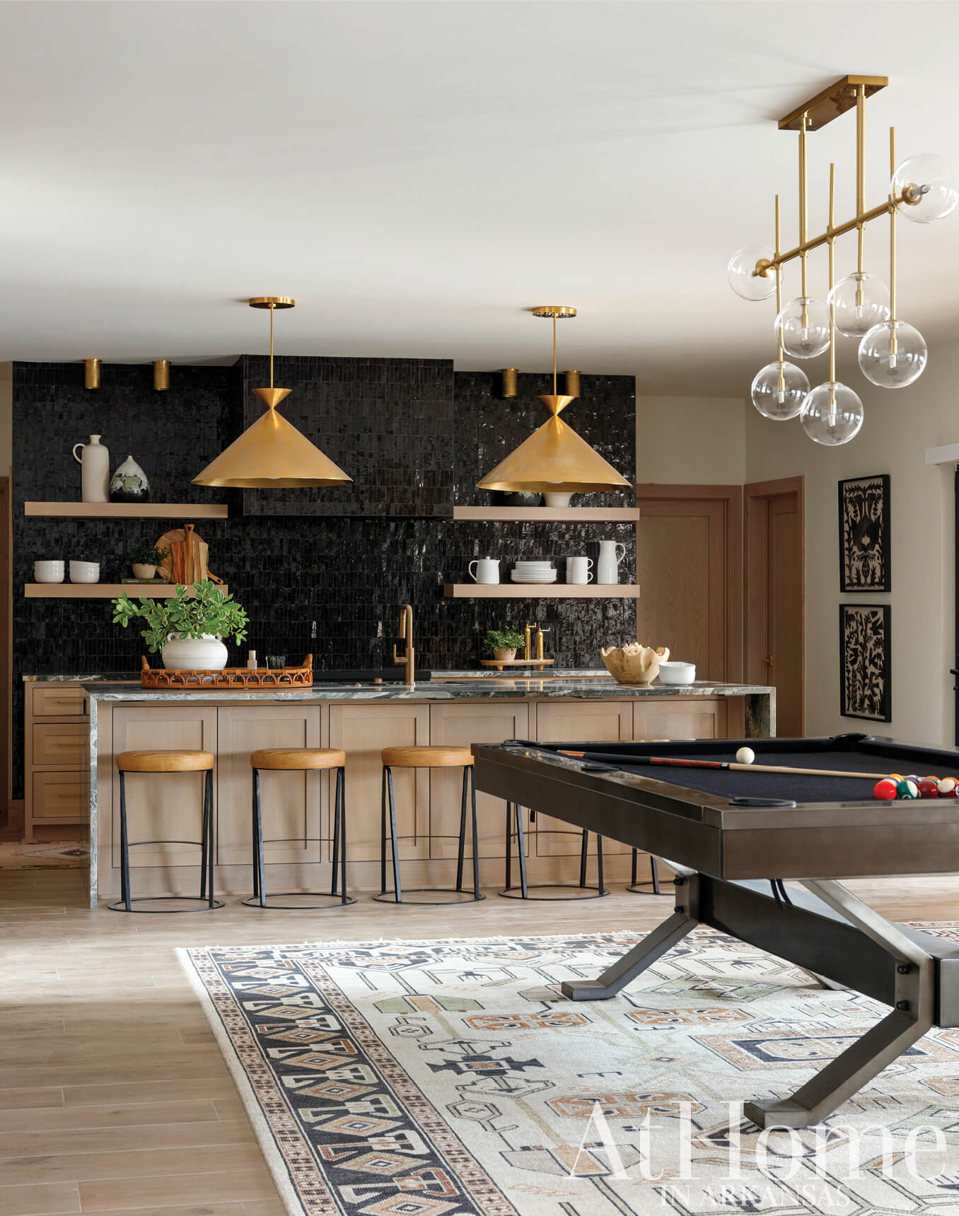 Modern kitchen with black tile backsplash, gold pendant lights, and a pool table.