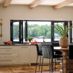 White kitchen with wooden beams, black windows, and a view of the lake.