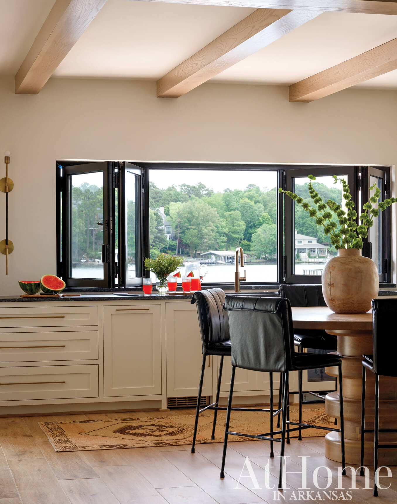 White kitchen with wooden beams, black windows, and a view of the lake.