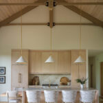 Light wood kitchen with island, pendant lights, and upholstered chairs.