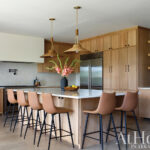 Wooden kitchen cabinets, island, and bar stools with teal tile backsplash.