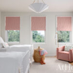 Pink roman shades, white bedding, and a window view.