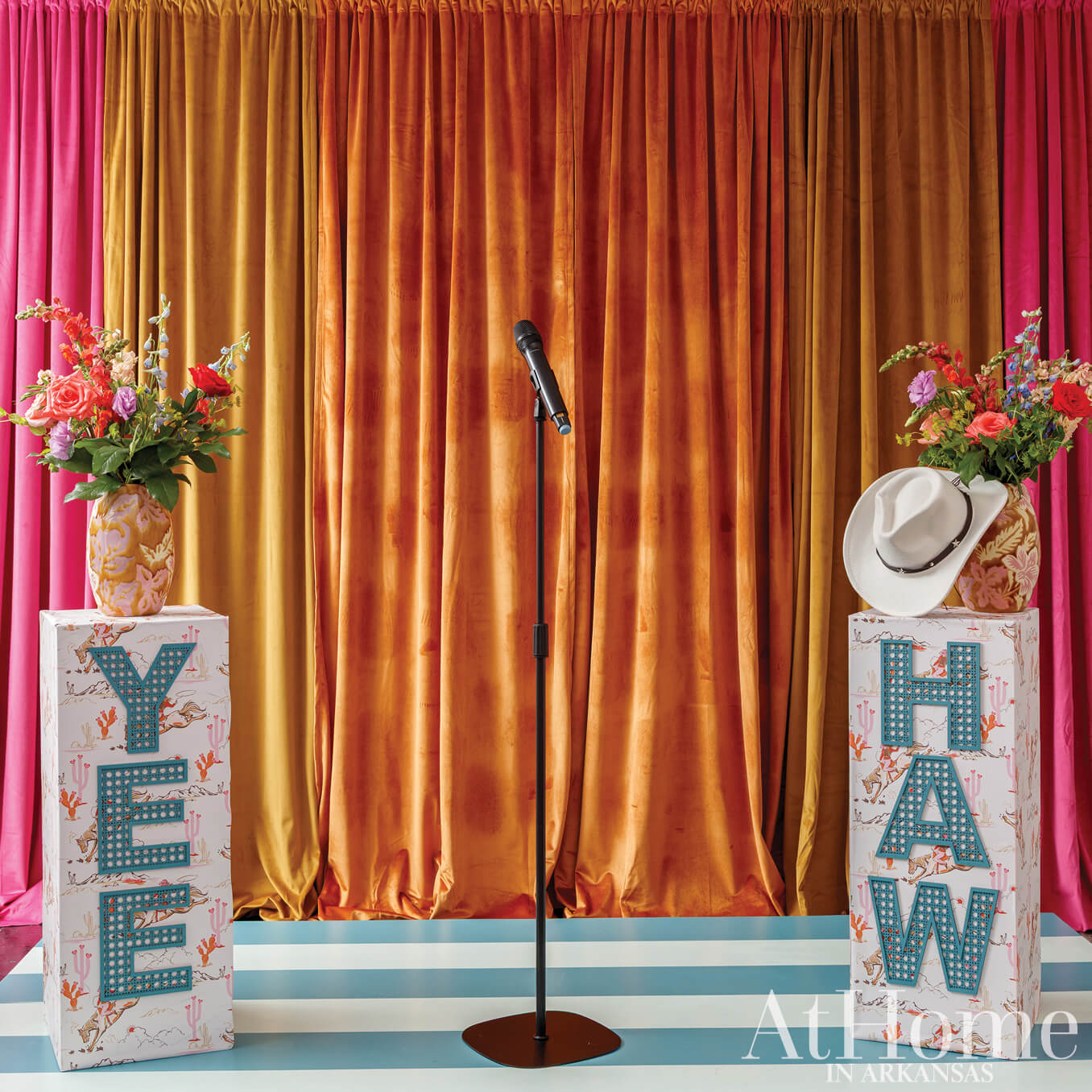 Stage with orange curtains, floral arrangement, microphone, and signage.