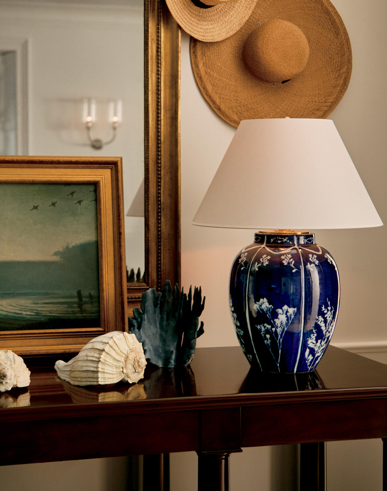 Dark wood console table with lamp, shells, and artwork.
