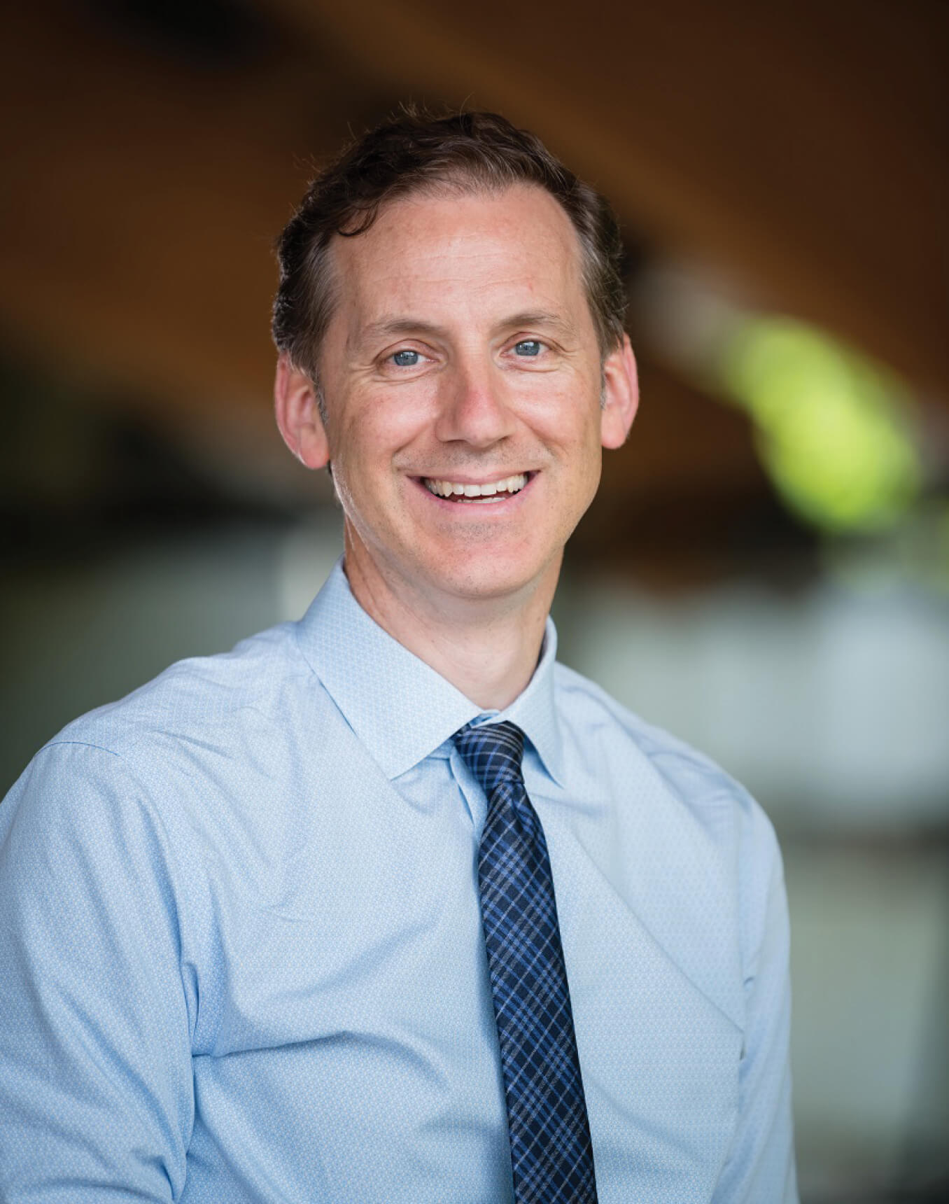 Man in a blue patterned shirt and tie smiling.