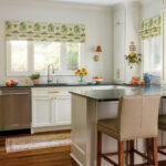 White kitchen with green patterned roman shade and black countertop.