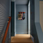 Dark blue, ribbed wall corridor with wooden stairs and a coat rack.