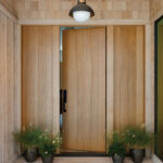 Wooden entrance doors with a pendant light and potted plants.