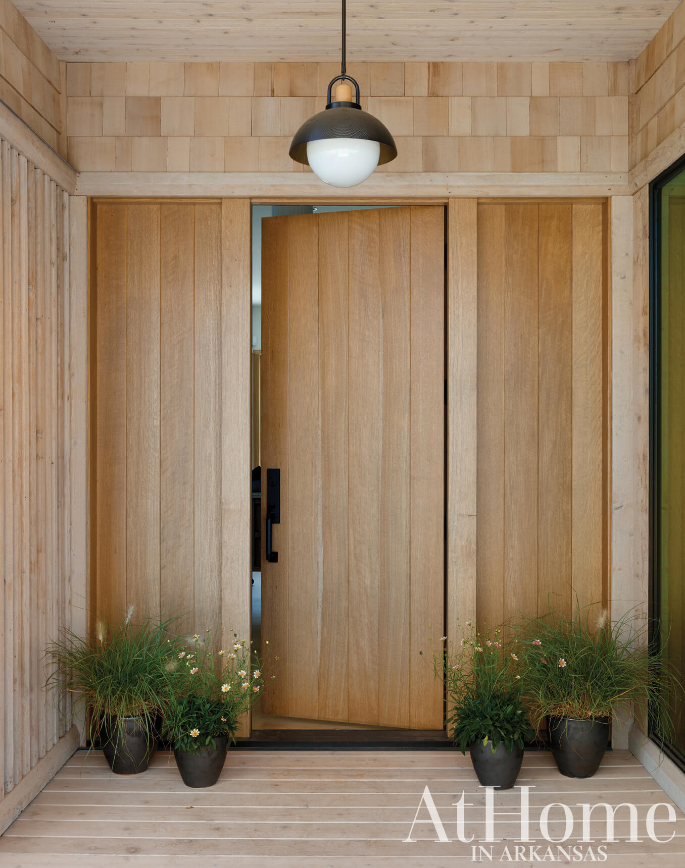 Wooden entrance doors with a pendant light and potted plants.