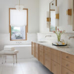 White marble vanity with wooden drawers and fixtures, featuring a window and bathtub.