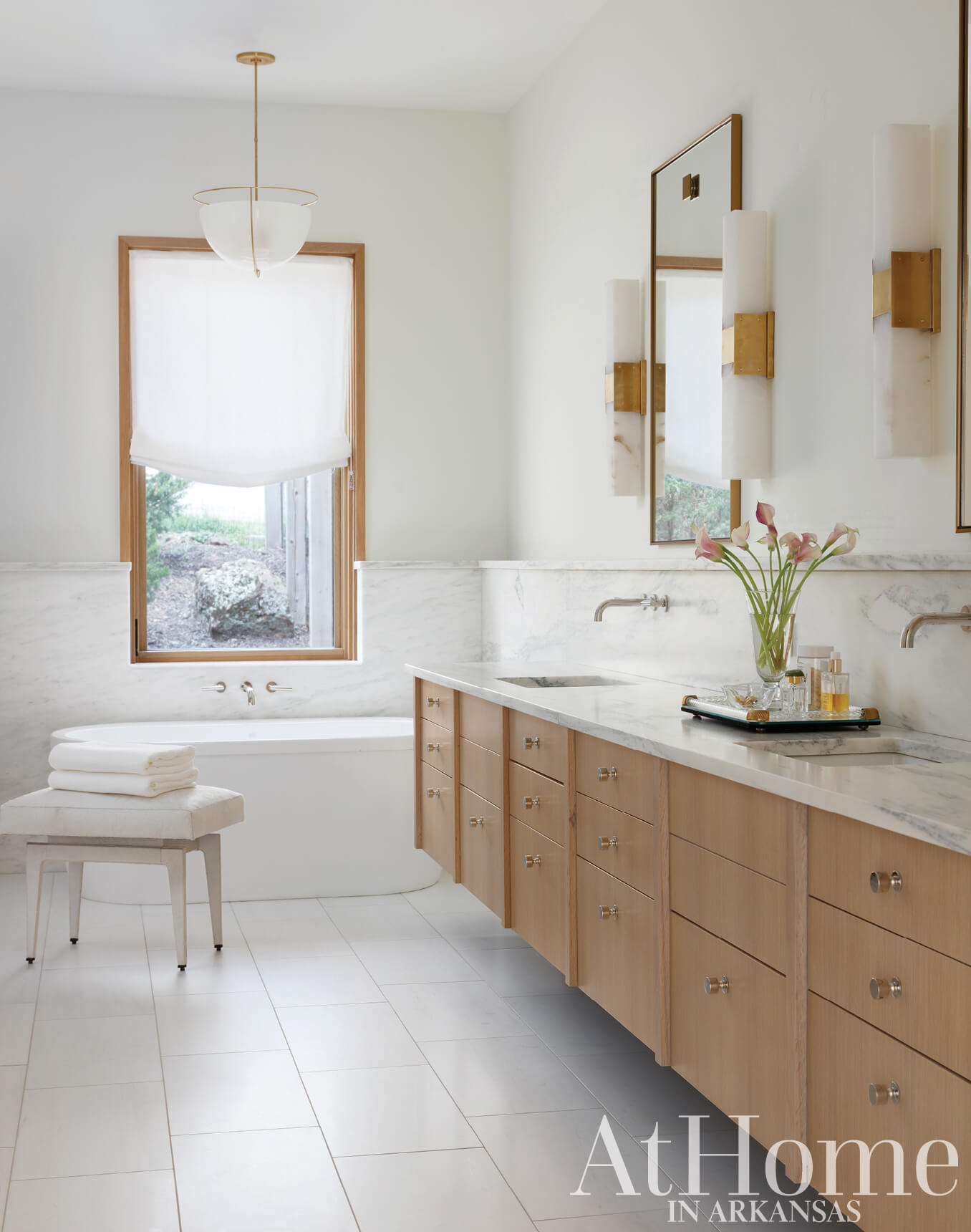 White marble vanity with wooden drawers and fixtures, featuring a window and bathtub.