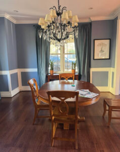 Blue dining room with a chandelier, wooden table, and patterned curtains.