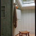 Green tile shower with wooden bench and towel rack.