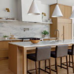 White marble kitchen island with wooden stools and pendant lights.