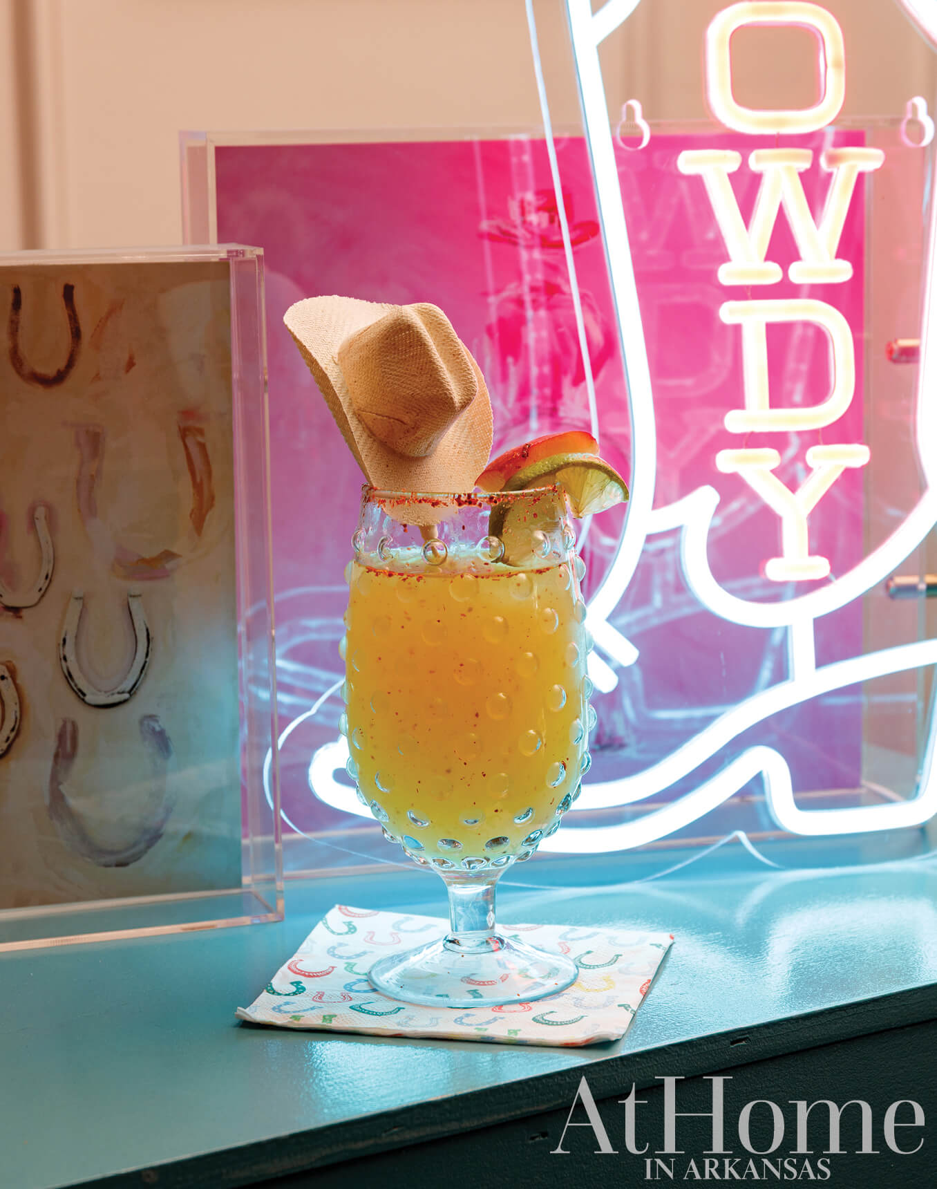 Yellow cocktail with lime garnish in a glass, neon sign, and magazine cover.
