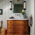 Wooden dresser with marble sink and mirror in a paneled bathroom.