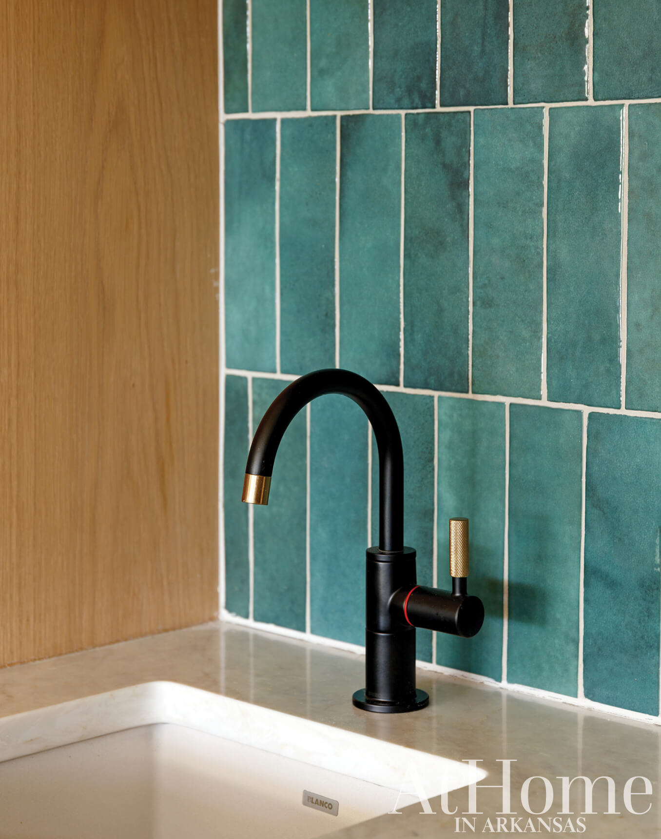 Teal ceramic tiles with a dark brass faucet and wooden countertop.