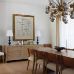 Wooden dining table with brass chandelier and artwork.