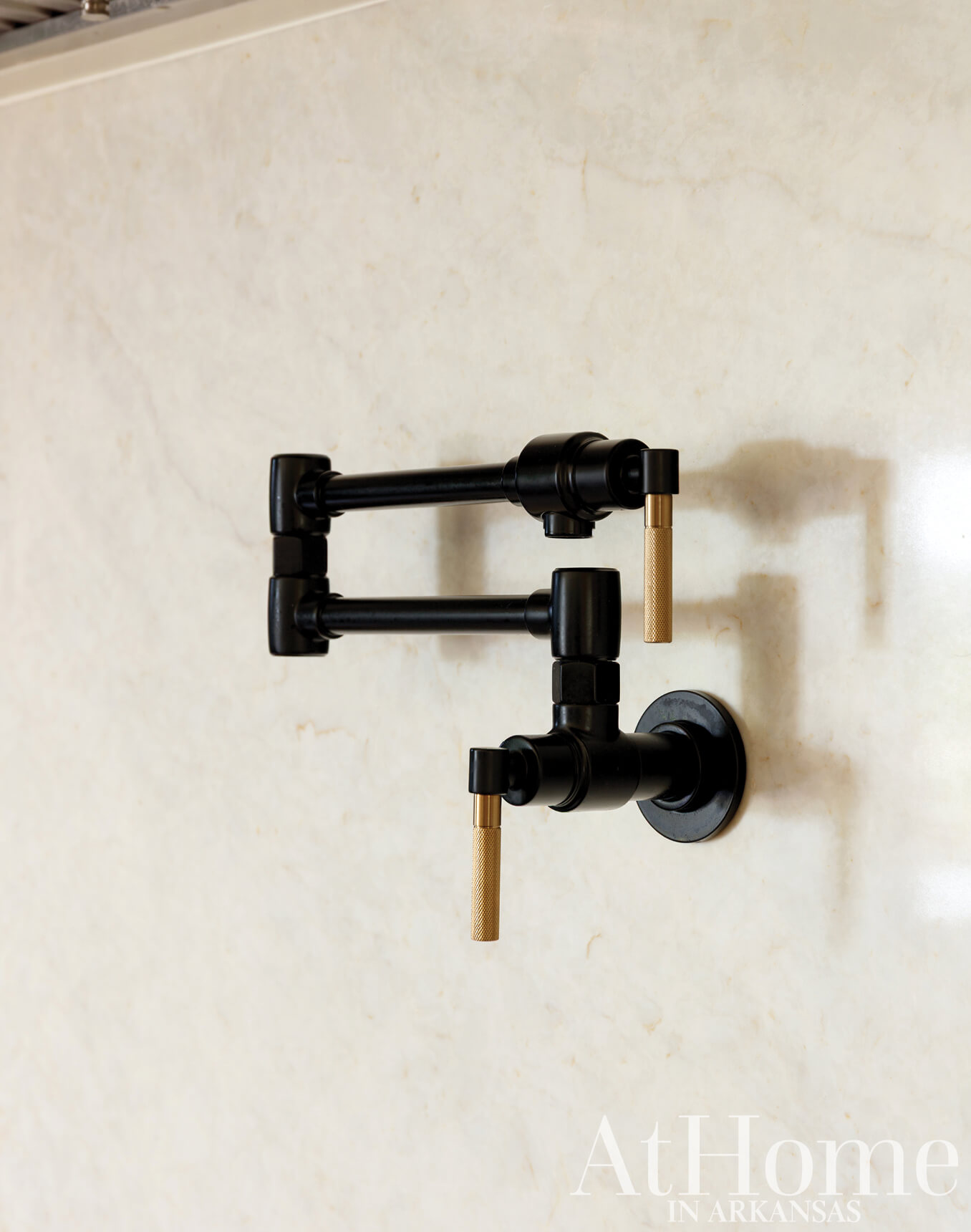Black and gold faucet on beige marble wall.
