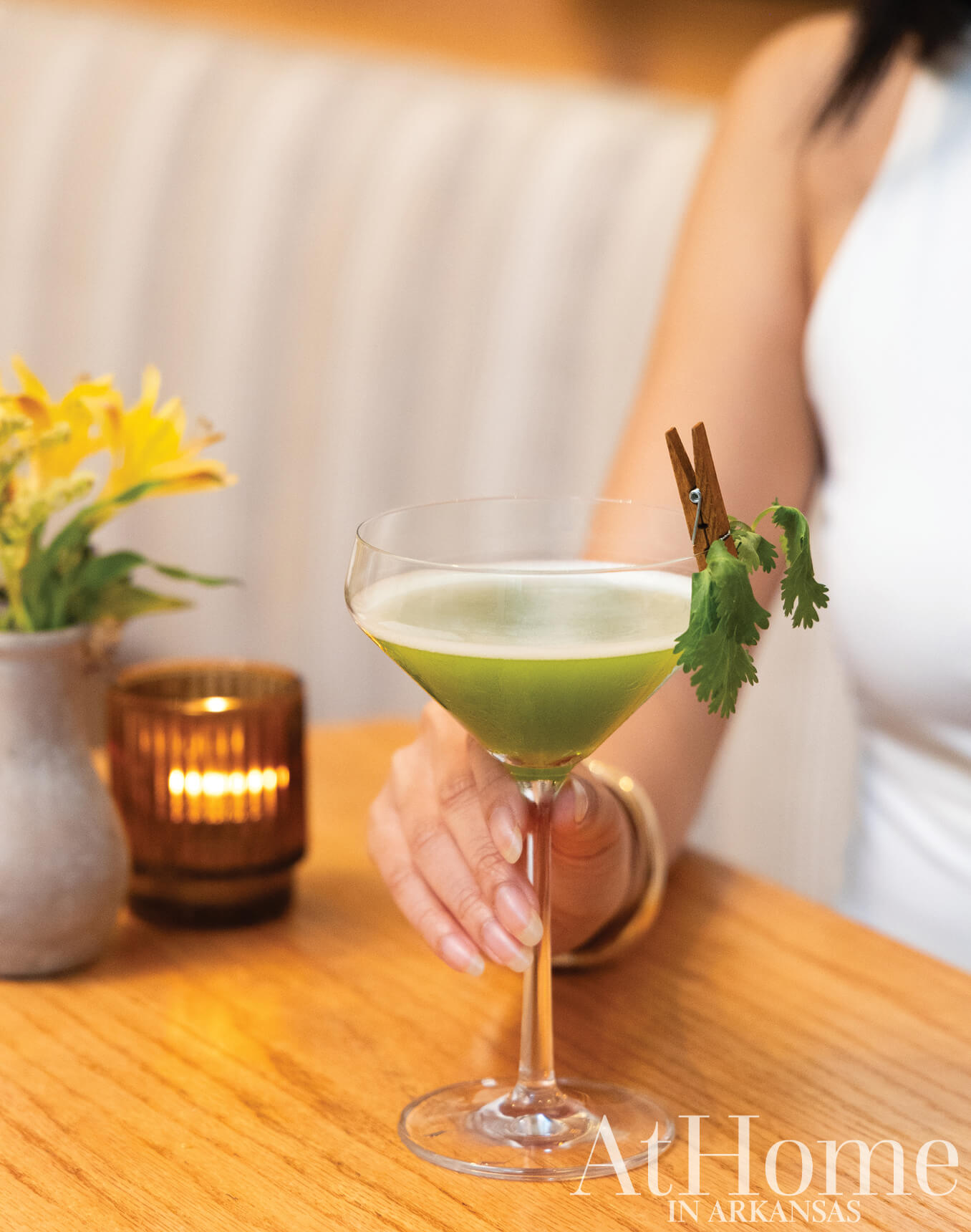 Green cocktail with cilantro and cinnamon stick on a wooden table.
