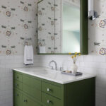 Green vanity with patterned wallpaper and mirror in a bathroom.