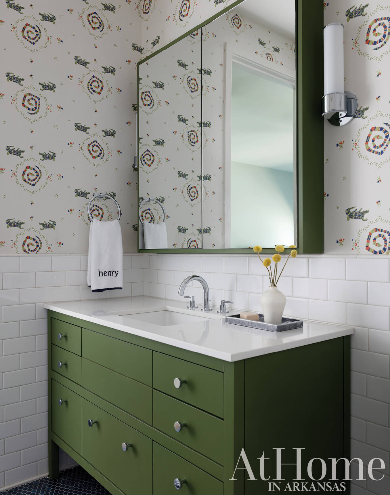 Green vanity with patterned wallpaper and mirror in a bathroom.