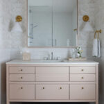 Pink vanity with mirror, sconces, and tile backsplash.
